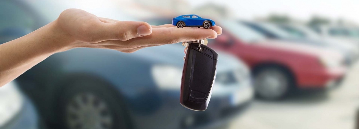 Hand met autosleutel en speelgoedauto met op de achtergrond auto's