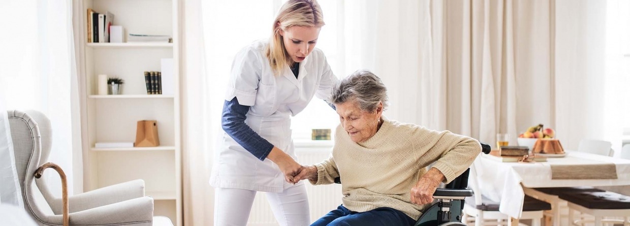 Een zorgmedewerkster helpt een oude dame op te staan vanuit haar rolstoel